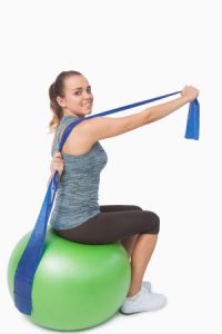 Woman sitting on a gym ball using a resitance band.